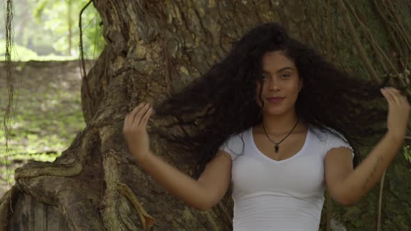 Close up of sexy young hispanic model playing in her hair standing in front of a large tree