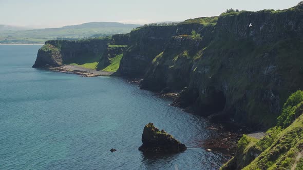 Lush Cliff Surrounded By Dark Blue Sea In Rathlin Island, Ireland With A Bird Flying On A Sunny Day 