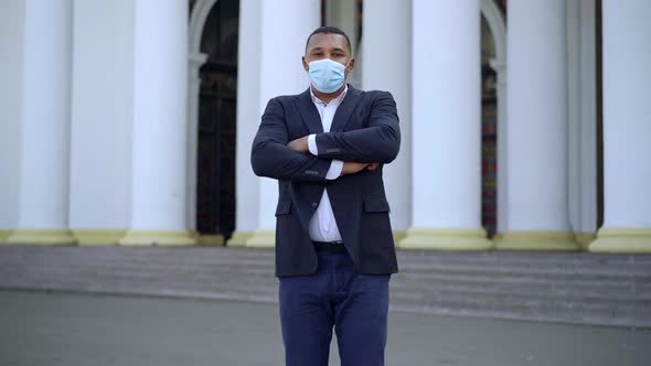 Confident Young African American Man in Suit and Covid Face Mask Crossing Hands Looking at Camera