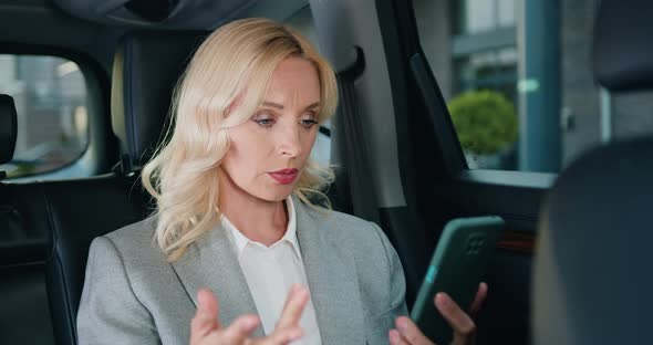 Middle Age Woman in Suit Talking by Video Call on Mobile Phone Sitting in the Car.