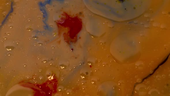 Abstract slow motion footage of a red droplet falling into colored, oily liquid