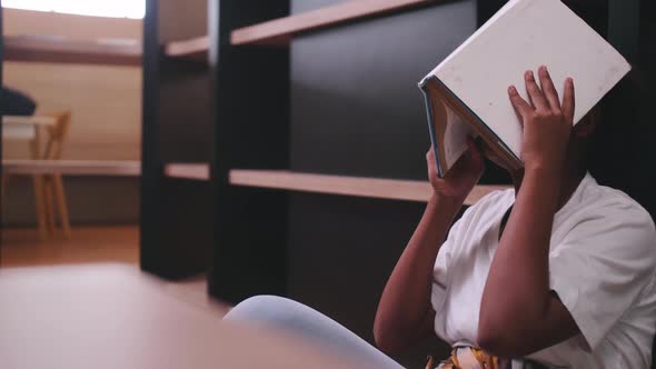 A schoolgirl is bored with reading books while preparing for exams while sitting in the library.