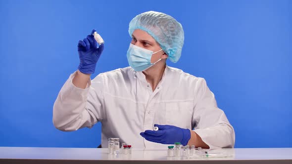 Healthcare Professional in a Protective Suit Mask and Gloves Examines Samples of Vaccine in Vials