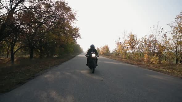 Front View of a Man in Black Helmet and Leather Jacket Riding Motorcycle on a Country Road