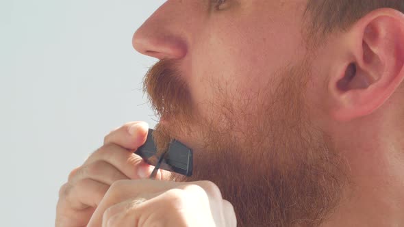 Adult man cutting his own beard and mustache with scissors comb Caucasian red bearded male face 4K