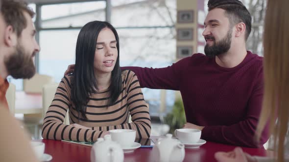 Portrait of Young Caucasian Couple in Love Hugging in Cafe. Happy Man and Woman Sitting with Friends