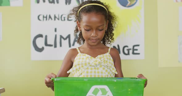 Video of happy african american girl holding box with recycling symbol in classroom