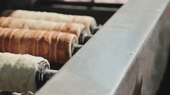 Changing one of the baking hungarian chimney cakes from others above the glowing ember.