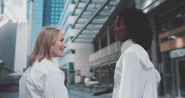 Two young women in business attire, talk and point towards a direction and smile