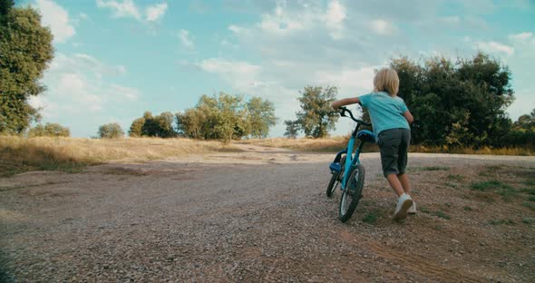 Child Boy Walk Holding Bicycle on Summer Vacation in Rural Environment