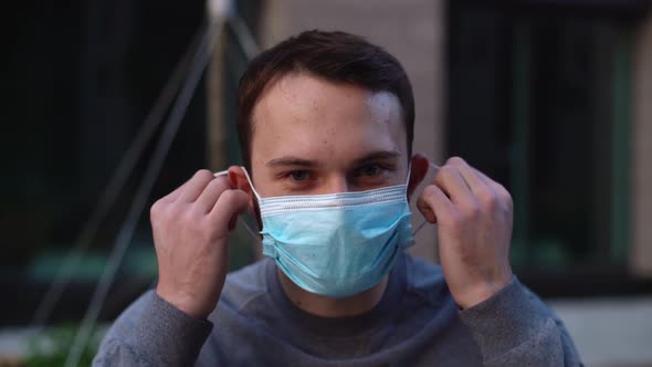 Close-up face of cheerful young man take off medical mask and smiling looking at the camera