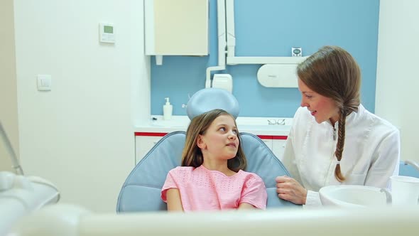 Friendly female dentist talking with cute girl before routine check up