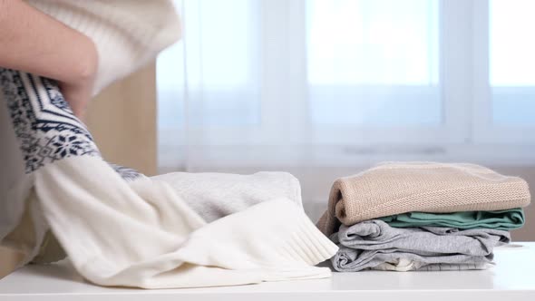 Woman Takes Sweater From Middle of Folded Clothes on Table