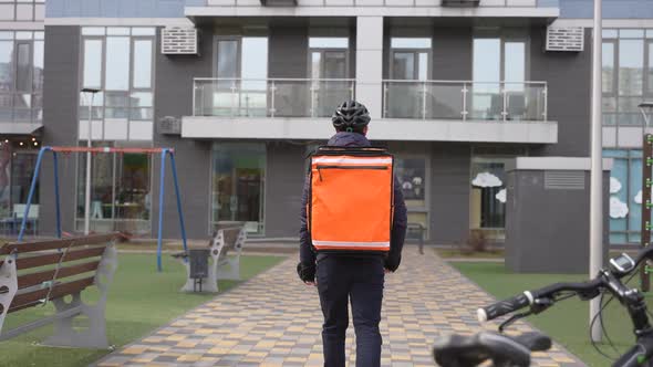 Courier with Thermal Backpack Walking to Building