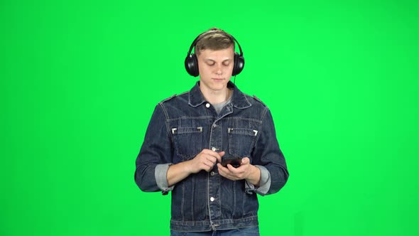 Man in Big Headphones Goes and Texting with Smartphone on Green Screen at Studio