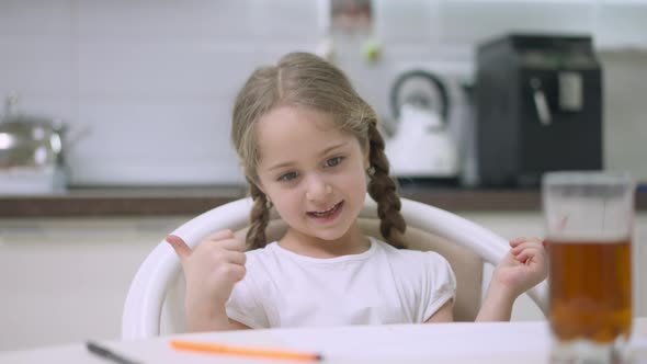 Charming Pretty Girl with Pigtails Drawing Sitting in Kitchen at Home