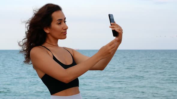 Beautiful sexy tanned woman makes selfie on the background of the sea. Woman makes summer photo