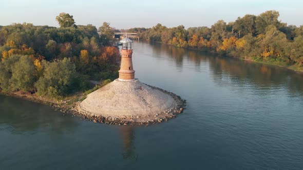 Aerial drone orbiting around the old stone lighthouse on the Danube river on a sunny autumn sunset d