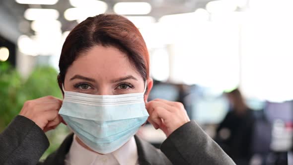 A Happy Woman in a Suit Walks Around the Office and Takes Off Her Medical Mask