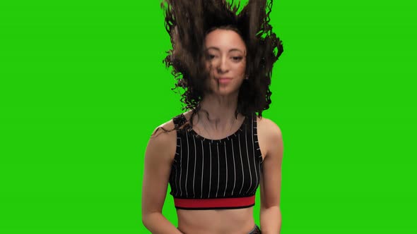 Attractive petite woman whips her long curly hair and dances on green screen