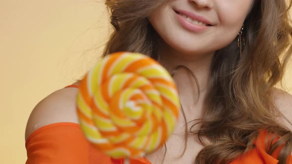 Cute girl with caramel candy on colored studio background