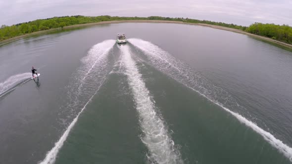 Aerial birds-eye drone view of a man wakeboarding behind a boat.