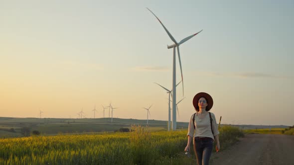 Happy tourist in a hat walking near a farm with alternative green energy windmills