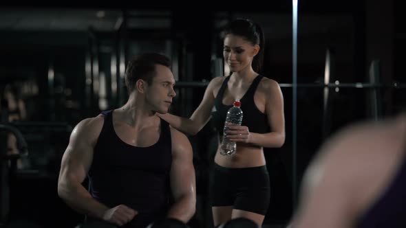 Attractive Sportive Woman Brings Bottle of Water to Bodybuilder After Trainings