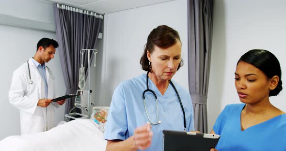 Nurses discussing over digital tablet while doctor checking a iv drip on patient