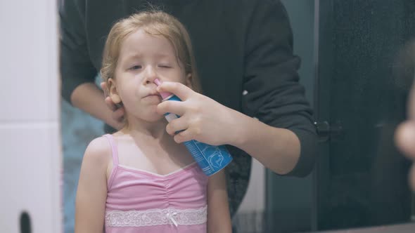 Mommy Irrigates Girl Nose with Nasal Spray at Large Mirror