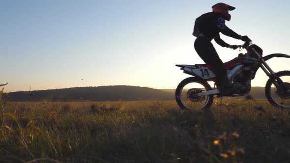 Two Motorcyclists Passing Through Field with Beautiful Sunset at Background. Warm Summer Sun Lights