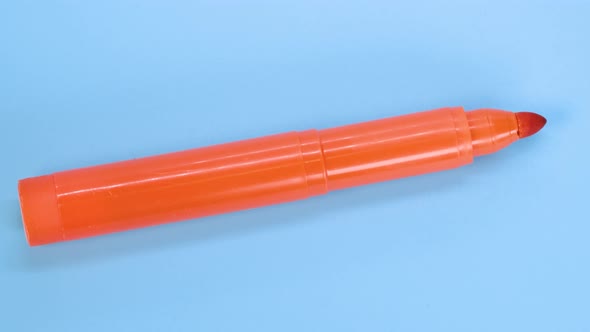 Orange marker pen rotating on blue surface background, macro shot close up view detail.