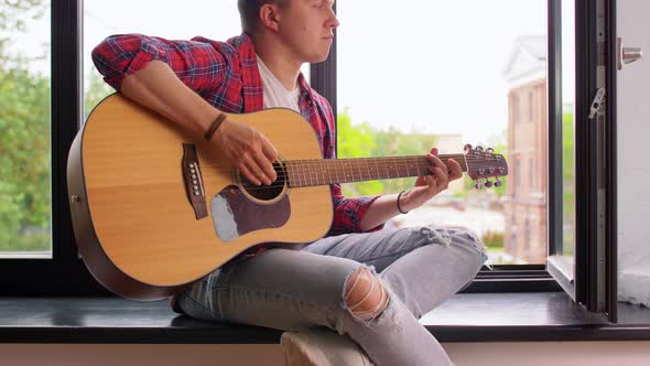 Young Man Playing Guitar Sitting on Windowsill