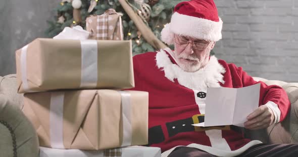 Portrait of Concentrated Old Santa Claus Reading Letter. Mature Man with White Beard in Eyeglasses