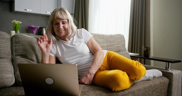 Happy Grandmother Video Conferencing on Her Laptop Computer with Her Family Smiling and Waving As