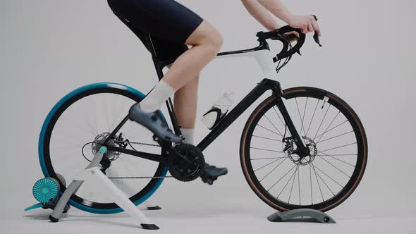 Shot of the Legs of a Cyclist Training on an Exercise Bike in White Studio