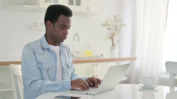 Excited African Man Celebrating Success on Laptop at Home 