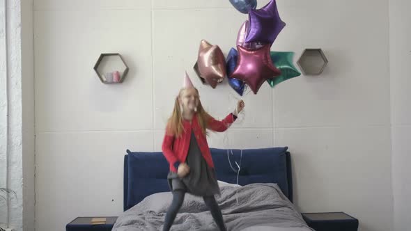 Teen Girl Jumping on Bed with Baloons on Birthday