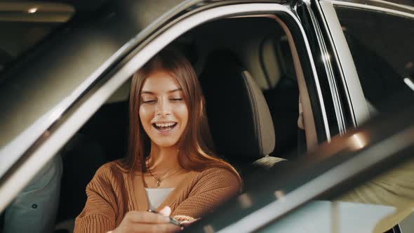 Happy Woman Taking Car Key From Dealer in Auto Show or Salon