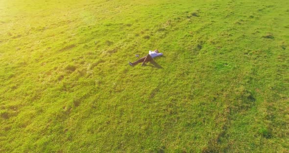 Low Orbital Flight Around Man on Green Grass with Notebook Pad at Yellow Rural Field