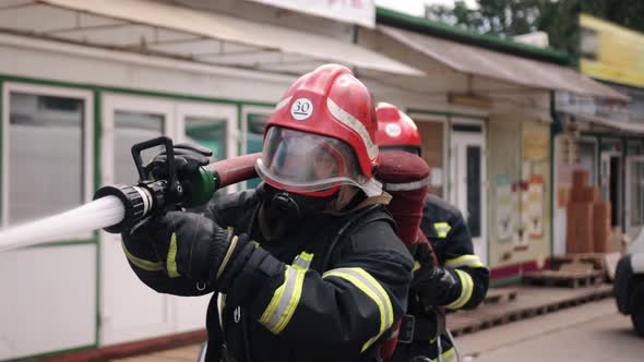 A Firefighter Fighting a Fire Truck in the Background and the Pressure of Water From Hose