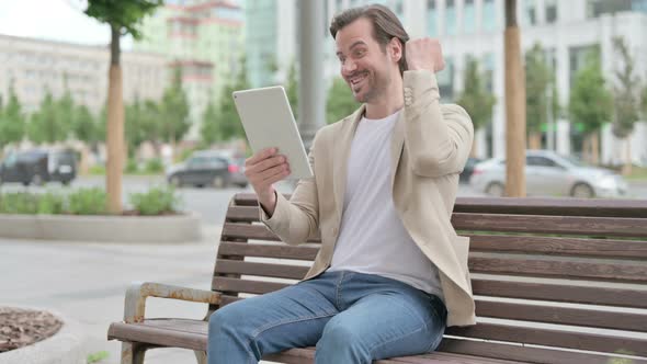 Young Man Celebrating Online Win on Tablet While Sitting on Bench