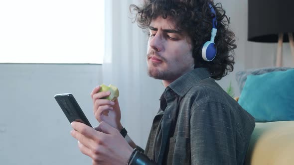 Young Man Listening to the Music and Gesturing While Eatting an Apple