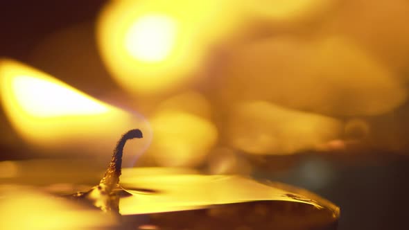 Static macro shot of a candle with a glowing flame - background candles shimmer with golden bokeh