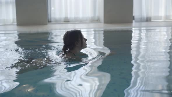 Side View of Young Caucasian Girl Swimming in Indoor Basin. Camera Following Confident Brunette