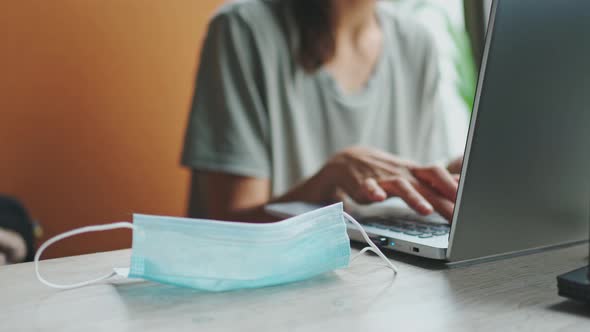 Used Protective Medical Mask Is on Table at Workplace and Woman Using Laptop