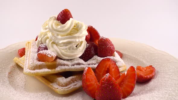 Belgian waffles with strawberry, whipped cream and powdered sugar on a plate on a white background.