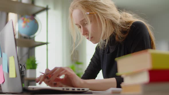 Young Blonde Woman Looking for Information on the Internet While Sitting at a Desk at Home While