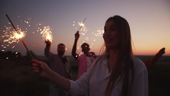 Happy people are dancing with big sparklers. Emotional woman in white shirt in closeup