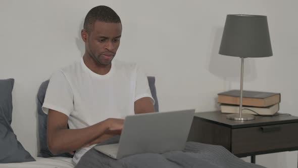African Man with Laptop Thinking While Sitting in Bed